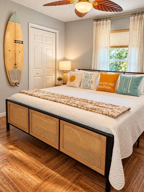 A bedroom with a bed, a ceiling fan, a surfboard, and a window with curtains. - Endless Summer Surf Shack 4 min to beach Walk to Restaurants (Panama City Beach)