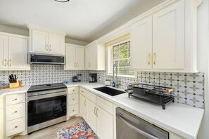 A kitchen with white cabinets, a microwave, an oven, a sink, and a dish rack. - Serene 4-bedroom house with AC in charming Spring TX 77386 (Spring)