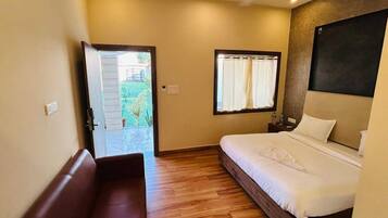 Habitación de hotel con cama, piso de madera, un banco, una ventana con cortinas y una puerta que da al exterior.