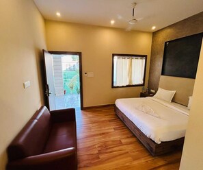 A hotel room with a bed, a wooden floor, a bench, a window with curtains, and a door leading outside. - Deluxe Red Chilly 3.O (Gorakhpur)