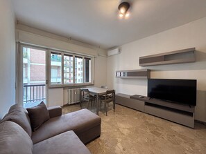 A living room with a sofa, a TV, a dining table, and chairs. - New Listing (Verona)