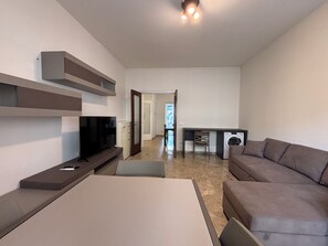 A modern living room with a flat-screen TV, a sofa, a dining table, and a washing machine. - New Listing (Verona)