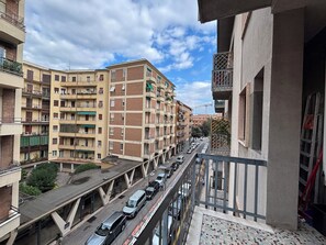 Un immeuble résidentiel à plusieurs étages, doté de balcons, d’une promenade piétonne couverte et de voitures garées dans la rue.