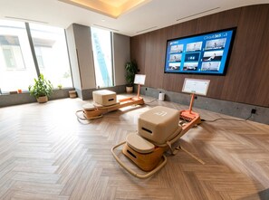 A modern room with two massage chairs, a large wall-mounted TV displaying fitness content, and a wooden floor. - Comfortable 1-Bedroom Stay in Toronto | Elm Ledbury (Toronto)