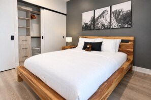 A bedroom with a wooden bed, white bedding, a nightstand with a lamp, a closet with sliding doors, and three framed pictures on the wall. - Comfortable 1-Bedroom Stay in Toronto | Elm Ledbury (Toronto)