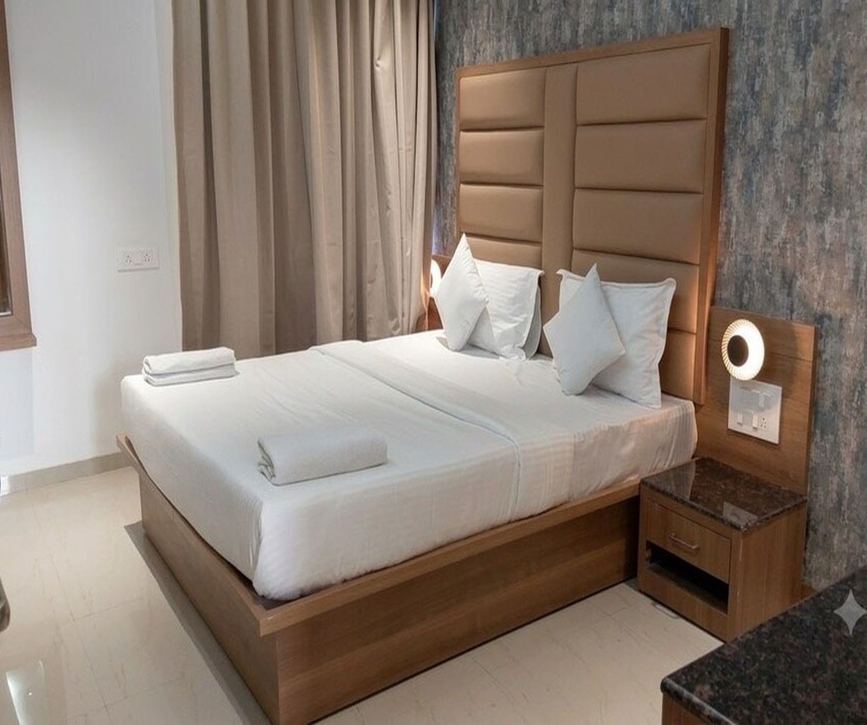 A hotel room with a wooden bed frame, white bedding, and a nightstand with a lamp.