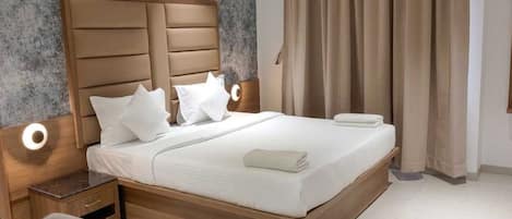 A modern bedroom with a large bed, wooden headboard, and a bedside table with a lamp.
