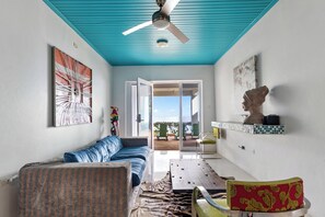 A room with a blue ceiling, a ceiling fan, a sofa, a dining table, chairs, and artwork on the walls. - Morgan’s cliff ocean front villa (Salt Gut)