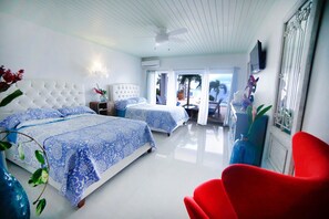 A hotel room with two beds, a red chair, and a view of the pool area. - Morgan’s cliff ocean front villa (Salt Gut)