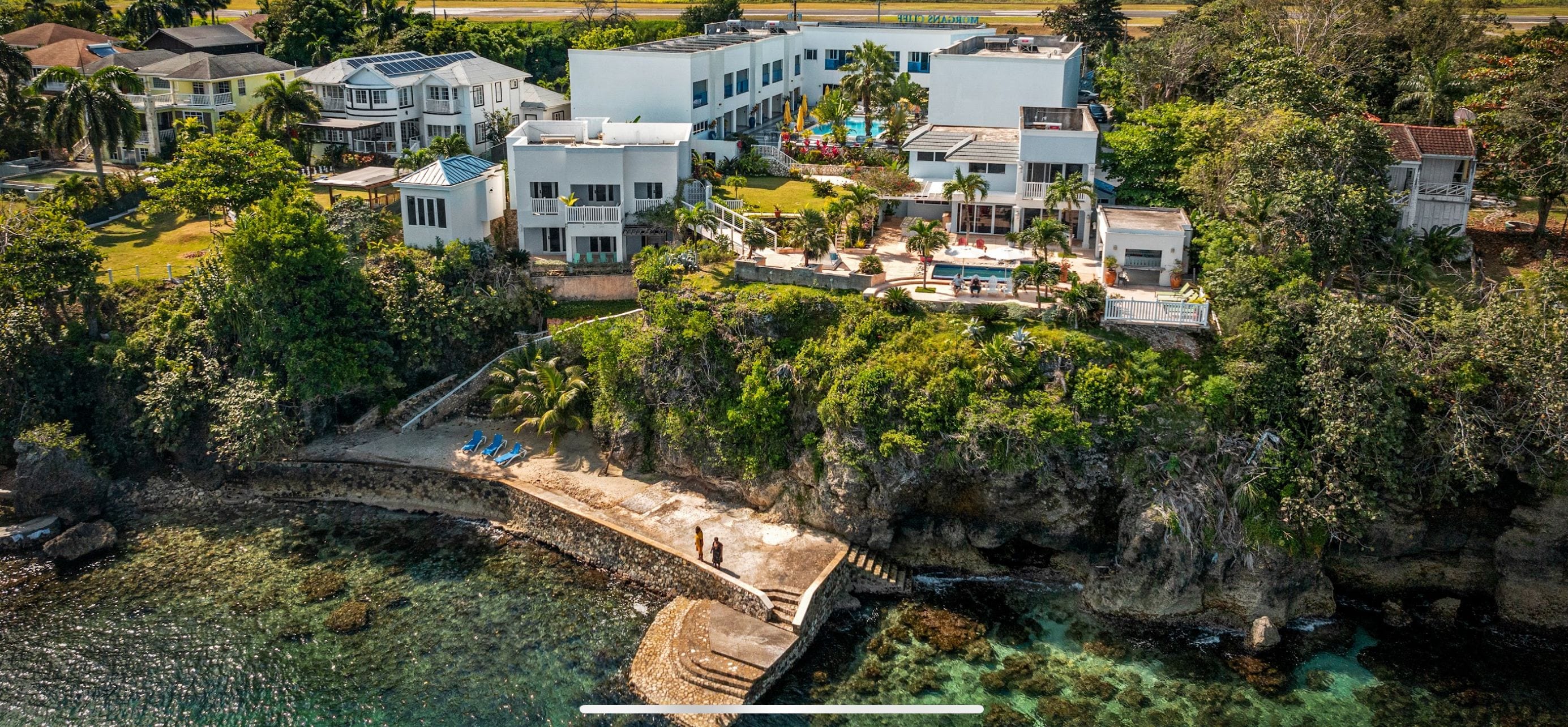 A coastal hotel with multiple buildings, a swimming pool, and a rocky shoreline.
