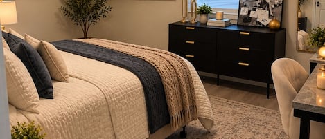 A bedroom with a bed, bedside table, dresser, TV, and a window with blinds.