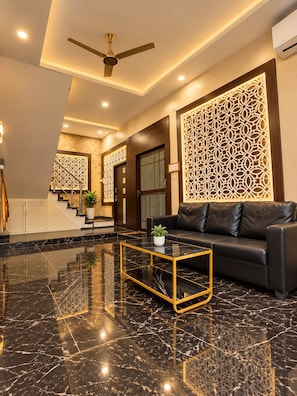 A modern lobby with a black leather sofa, a glass coffee table, and a ceiling fan. - Arivoo. Hotel Green Leaf (Datia)