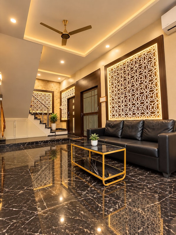 A modern lobby with a black leather sofa, a glass coffee table, and a ceiling fan.