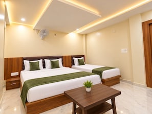 Una habitación de hotel con dos camas, una mesita de noche con una planta y un ventilador de techo.