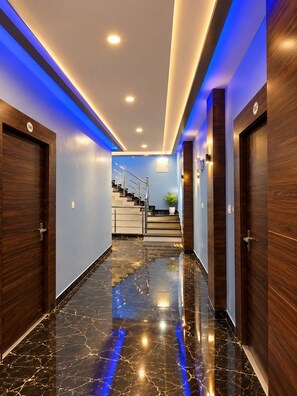 A hallway with wooden doors, a marble floor, and a staircase leading to an upper level. - Arivoo. Hotel Green Leaf (Datia)