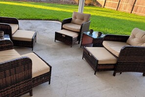 Een terras buiten met rieten meubels en kussens.