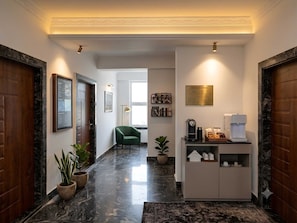 A hallway with marble flooring, wooden doors, a green armchair, a coffee station, and a framed informational sign. - Deluxe Room Raman Reti Resort (Krishnanagar)