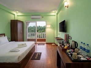 A hotel room with a bed, a TV, a balcony with a view, a desk with a tray of amenities, and a welcome mat. - Deluxe Room Raman Reti Resort (Krishnanagar)