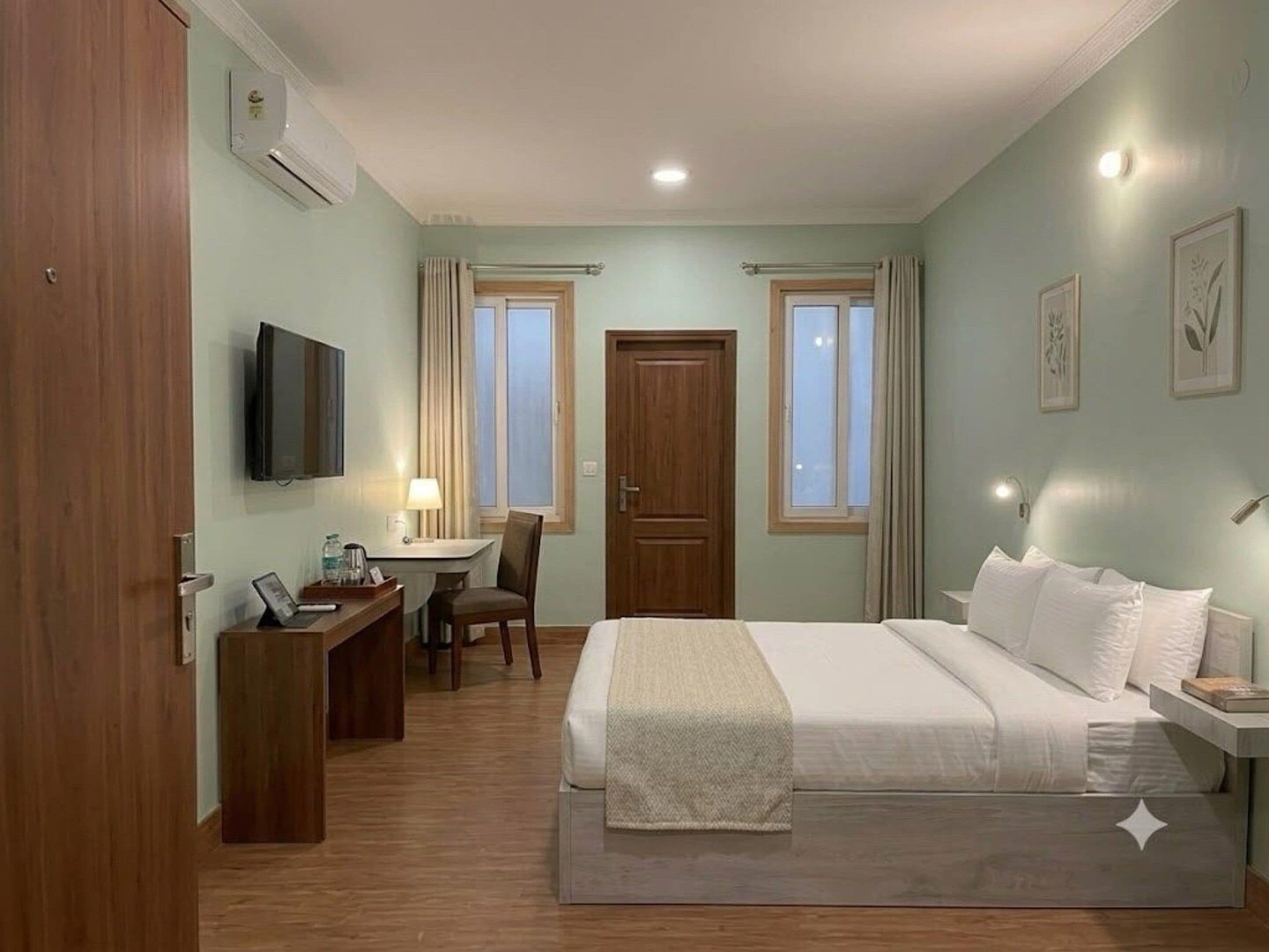 Una habitació d'hotel amb llit, taula de nit, escriptori, cadira, televisió i finestres.