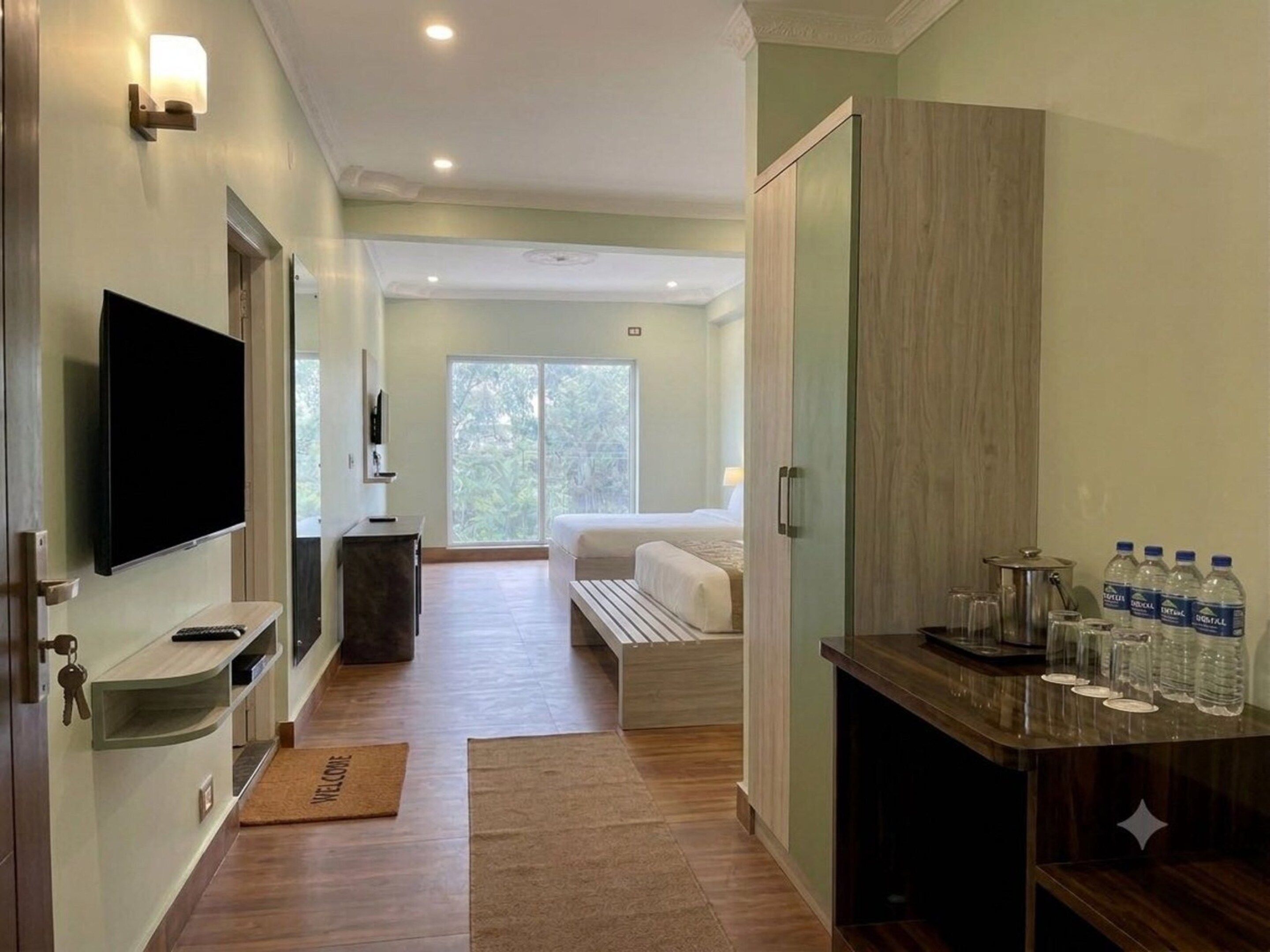 A hotel room with a bed, a TV, a desk with a computer, and a window with a view of trees.