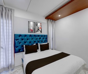 A bedroom with a tufted headboard, a bed with white and black bedding, and two framed pictures on the wall. - Deluxe sri Chendhoor's (Karur)