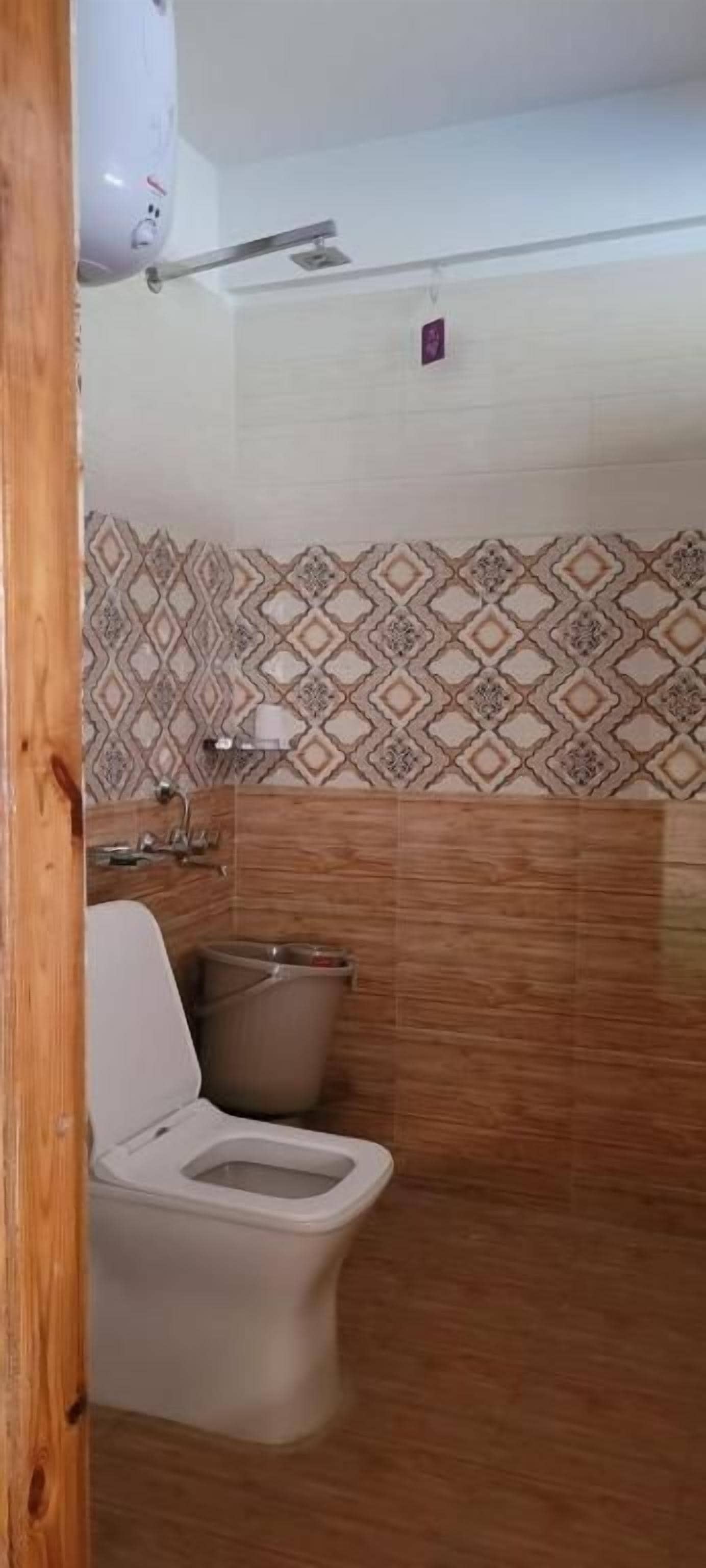 Un baño con inodoro, un cubo de basura y azulejos con diseño.