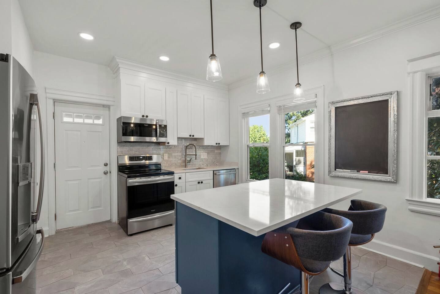 A modern kitchen with white cabinets, stainless steel appliances, a central island, and pendant lighting.