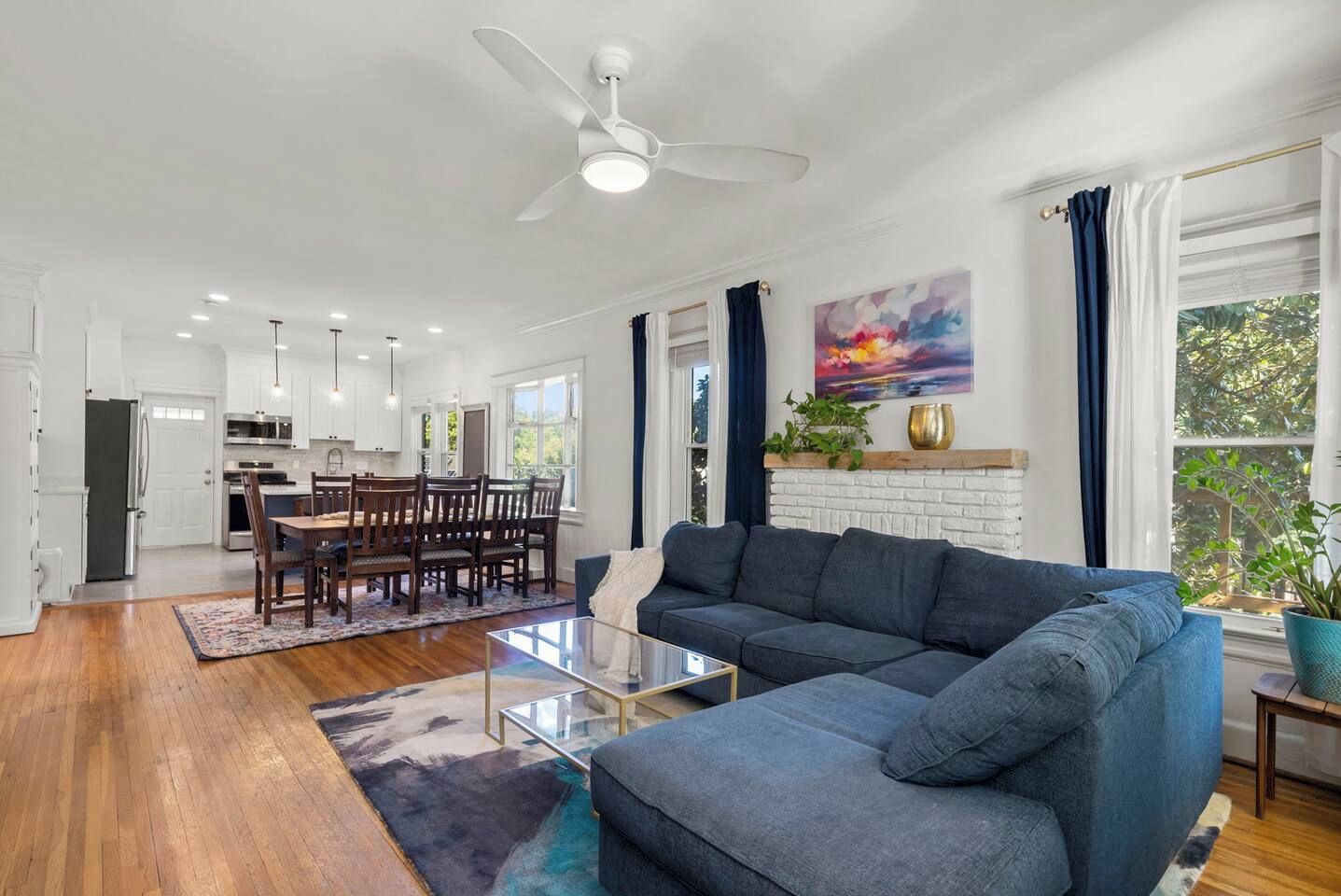 A spacious living area with a large sofa, a dining table with chairs, and a kitchen in the background.