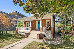 A two-story house with a covered porch, a blue door, and a brick exterior. - Magnolia Garden Home, Hot Tub, Private Garage, Walk to Metro, 4BR/4BA (Washington)