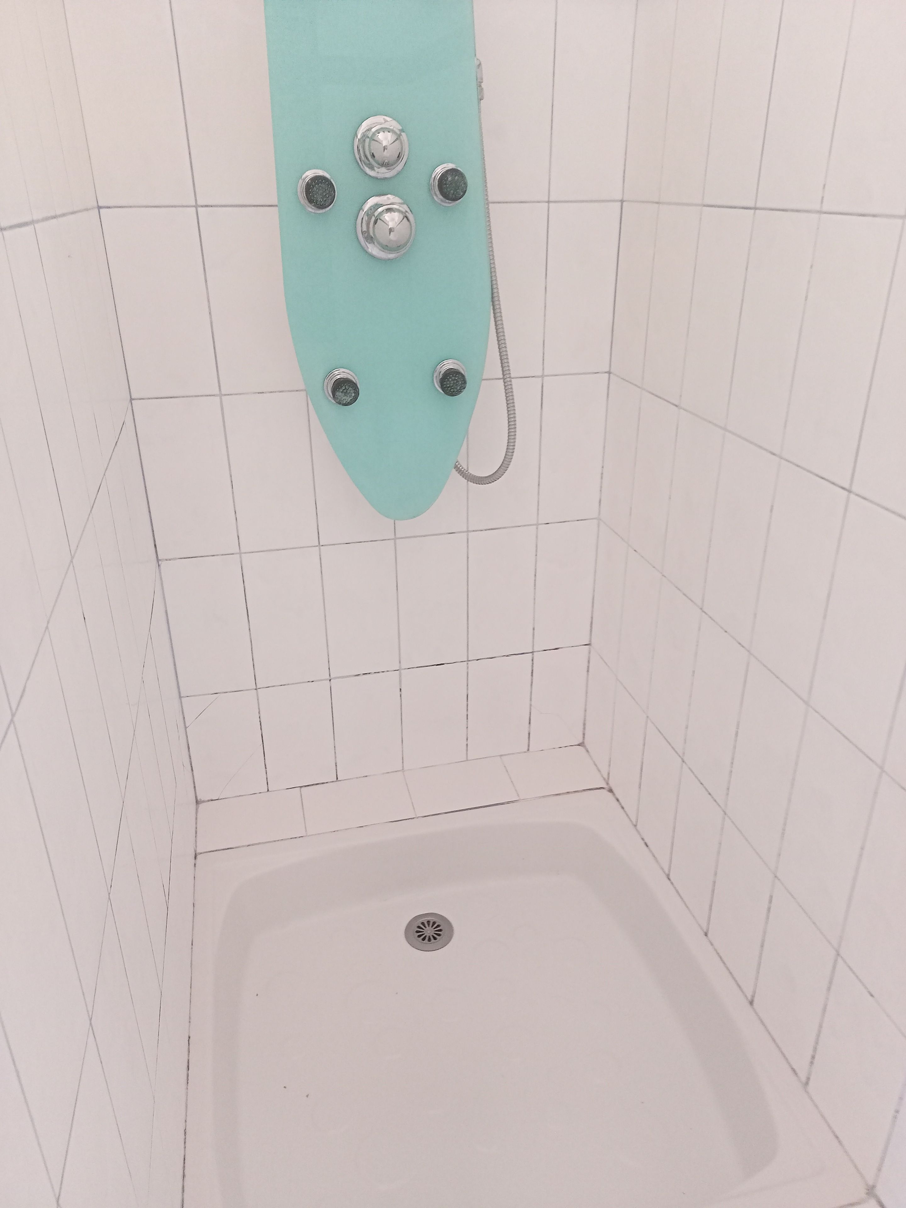 A small, tiled shower enclosure with a single showerhead and a handheld shower attachment.