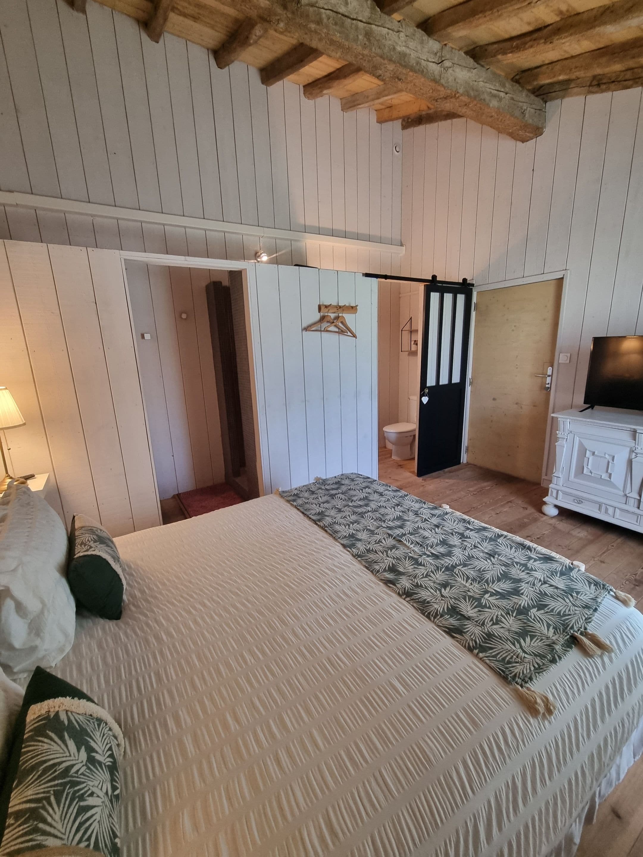 A bedroom with a large bed, wooden ceiling beams, a wardrobe, and a television.