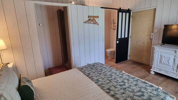 A bedroom with a large bed, wooden ceiling beams, a wardrobe, and a television.