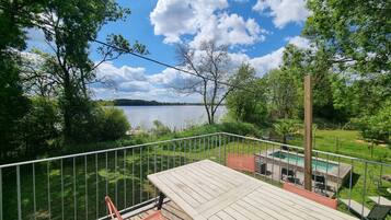 Eine Terrasse mit Tisch und Stühlen mit Blick auf einen See, umgeben von Grünflächen und einem eingezäunten Poolbereich.