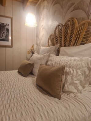 Cama com cobertura branca texturizada, vários travesseiros e cabeceira de fibra natural.