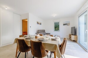 A dining area with a table set for four, a sofa, and a television on a stand. - Quartz - Jardin - Proche plage (Saint-Hilaire-de-Riez)