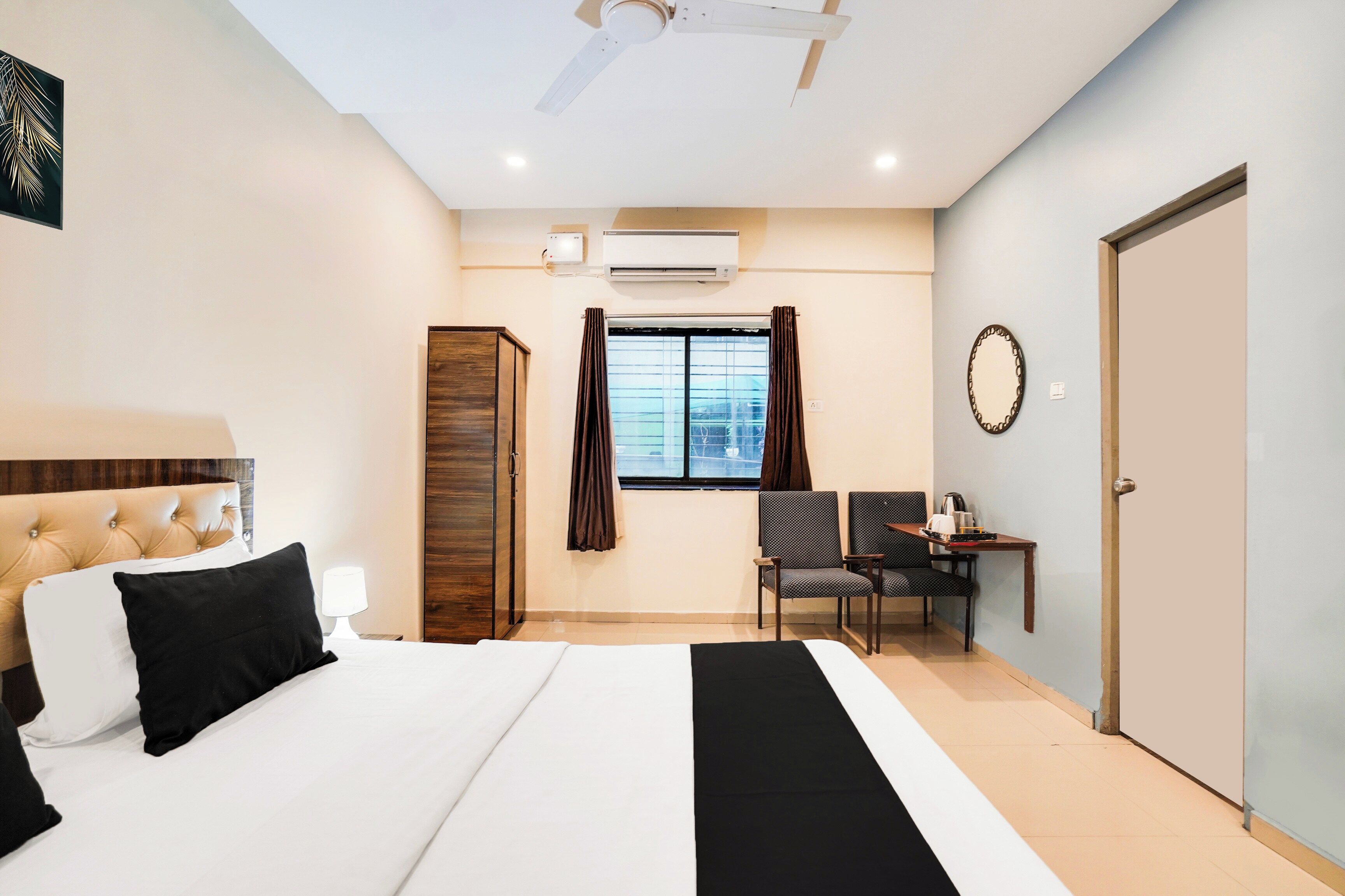 Habitación de hotel con cama, escritorio, silla, armario, ventana con cortinas, equipo de aire acondicionado y puerta.