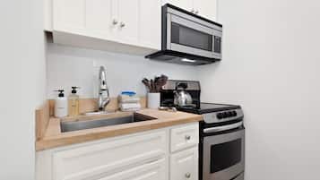 A kitchen with white cabinets, a stainless steel microwave, a stove, and a sink with soap dispensers.