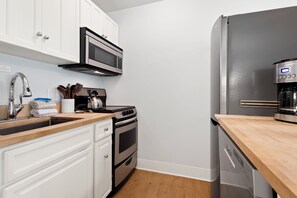 A kitchen with white cabinets, a stainless steel range, a microwave, a coffee maker, and a dishwasher. - Two Sisters Telluride (Telluride)