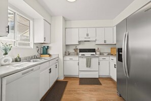 A modern kitchen with white cabinetry, a stainless steel refrigerator, a built-in oven, and a sink. - Your Home Away From Home - Cozy Retreat (Bakersfield)