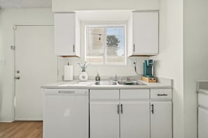 A kitchen with white cabinets, a window with blinds, a coffee maker, and a sink. - Your Home Away From Home - Cozy Retreat (Bakersfield)