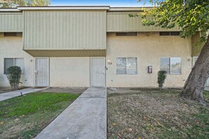 A two-story building with a flat facade, a central entrance, and a small front yard with grass and a tree. - Your Home Away From Home - Cozy Retreat (Bakersfield)