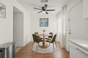 A dining area with a round table, four chairs, a ceiling fan, and a painting on the wall. - Your Home Away From Home - Cozy Retreat (Bakersfield)