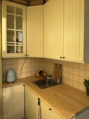 A kitchen with white cabinets, a sink, a kettle, and a bowl of fruit. - A travel-curated flat in the heart of Grünerløkka (Oslo)