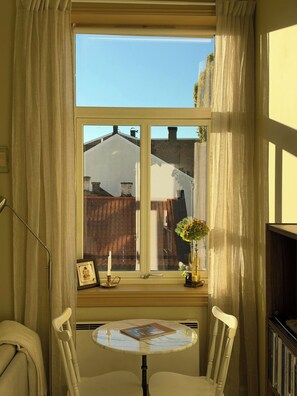 A room with a window, a small table, two chairs, a lamp, a picture frame, a candle holder, and a vase with flowers. - A travel-curated flat in the heart of Grünerløkka (Oslo)