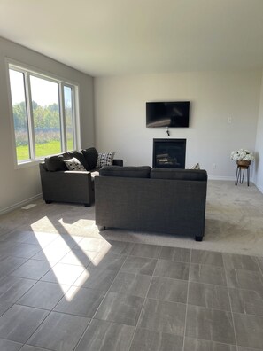 A living room with a grey sectional sofa, a flat-screen TV mounted on the wall, and a fireplace. - Ottawa Getaway | 4BR Home + Free parking +WI-FI (Ottawa)