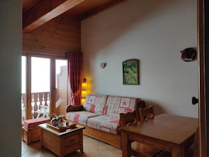 Ein gemütliches Wohnzimmer mit einer Holzsofa, einem Esstisch und einer Küchenzeile inklusive Wasserkocher und Tassen.