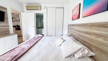 Un dormitorio con cama, cabecera de madera, mesita de noche, cómoda y baño visible a través de una puerta abierta.