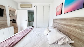 A bedroom with a bed, a wooden headboard, a nightstand, a dresser, and a bathroom visible through an open door. - SA - Clube XV - Apto CXV1004 (Santos)