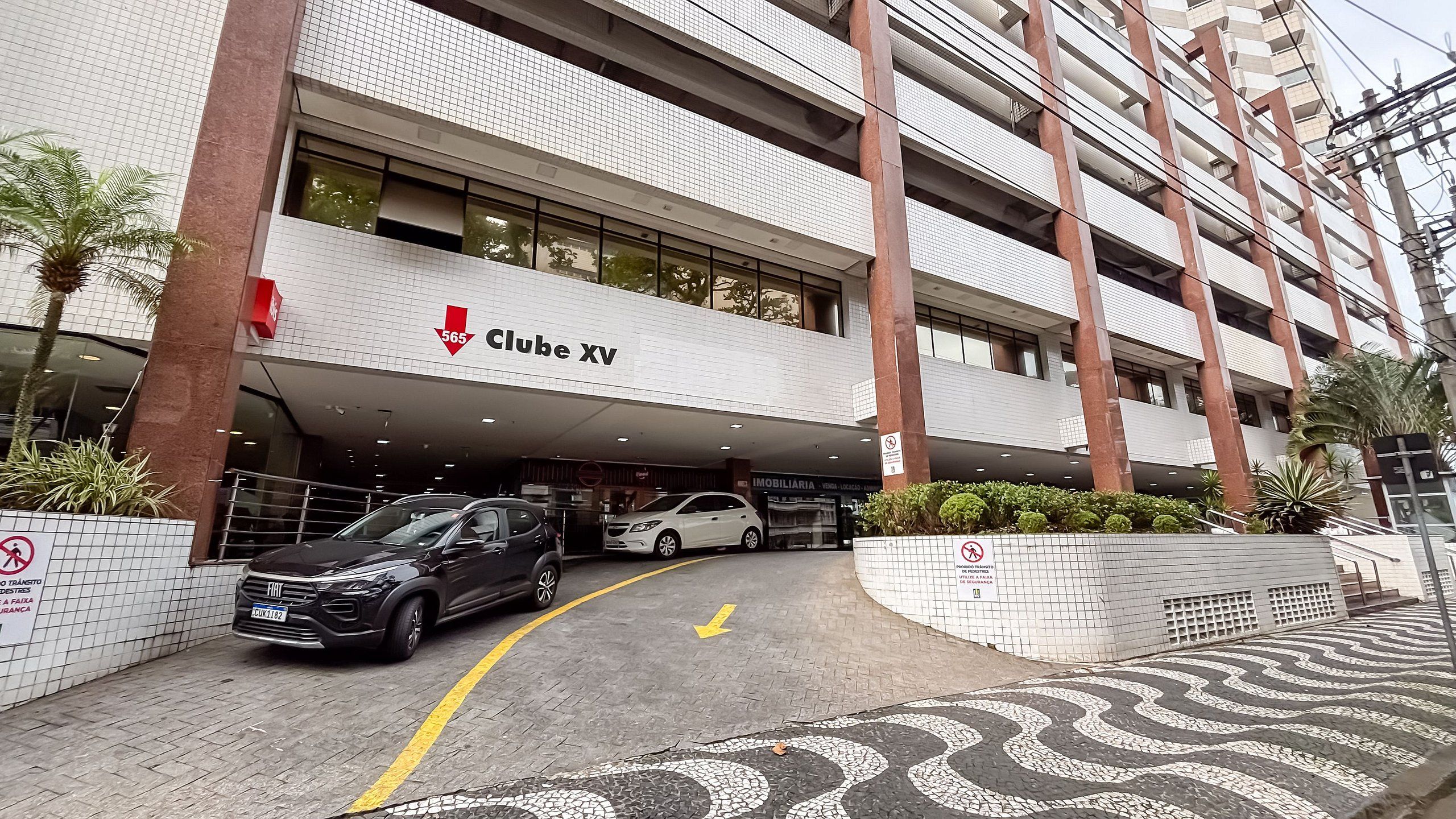 Un edificio moderno con un letrero que dice 'Clube XV' y un estacionamiento con dos coches.