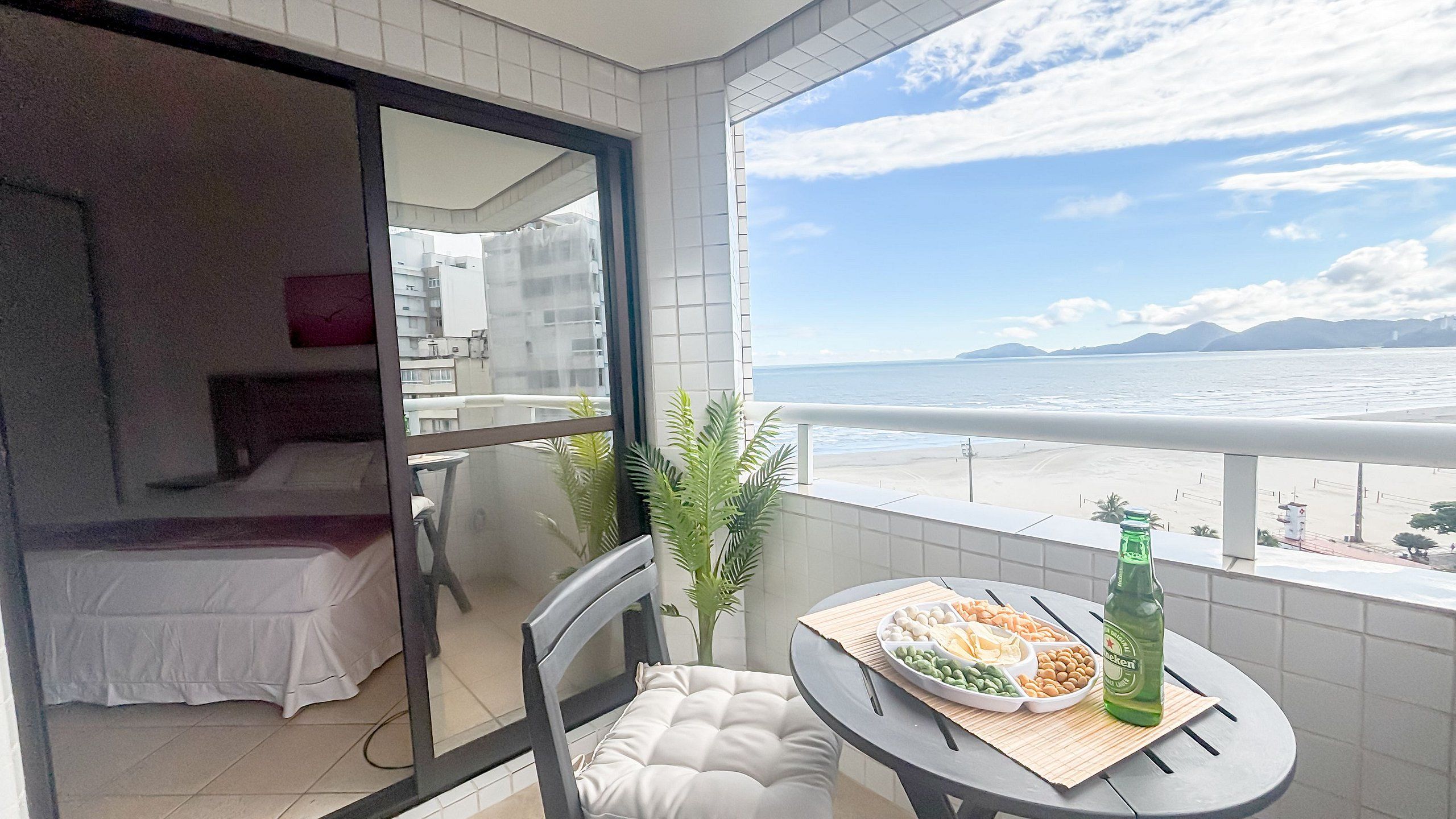 Uma varanda com uma mesa de jantar, uma garrafa e vista para o mar.